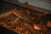 Fireglass amber en zwart onder de houtstammen van een Flamente elektrische haard