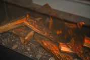 Luxe bodemdecoratie met verkoolde stenen onder de houtstammen van een Flamente elektrische haard